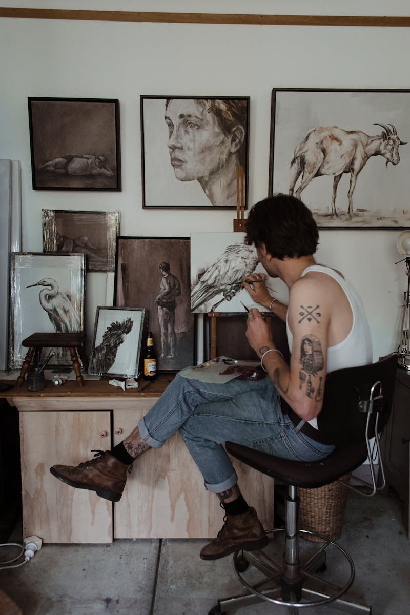 A young male artist painting in his studio, surrounded by various artworks and creative tools.