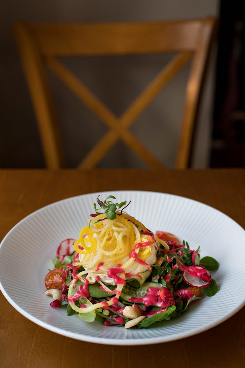 A vibrant gourmet vegan salad featuring spiralized vegetables, radishes, and leafy greens on a white plate.
